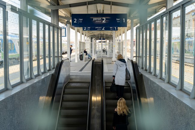 Podróżne wjeżdżają na nowy peron stacji Rzeszów Główny schodami ruchomymi. Nad nimi tablice informacyjne. fot. Szymon Grochowski